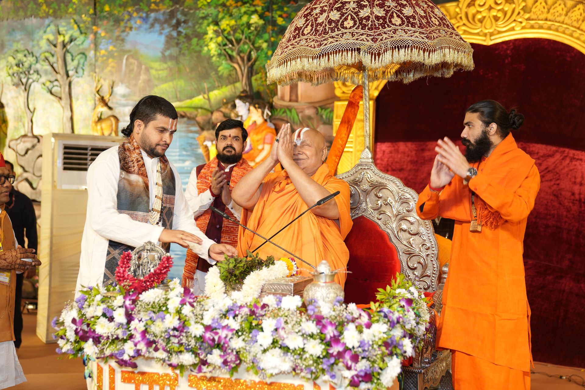 The Katha narrator and participants with joined palms beneath a ceremonial umbrella.