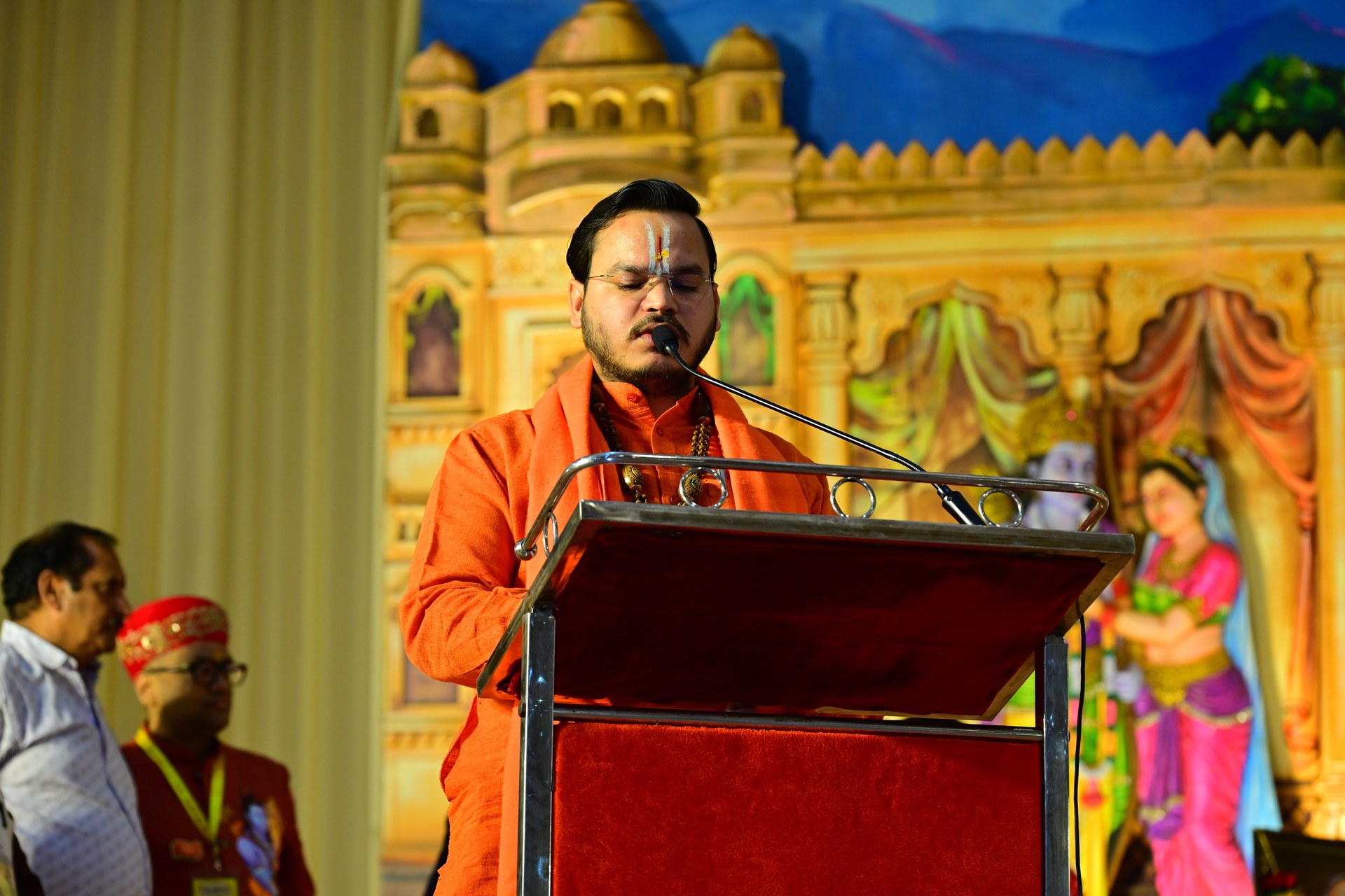 A speaker in orange attire addresses the gathering from a red lectern.